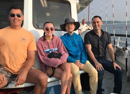 Four people sitting on a fishing boat, smiling.