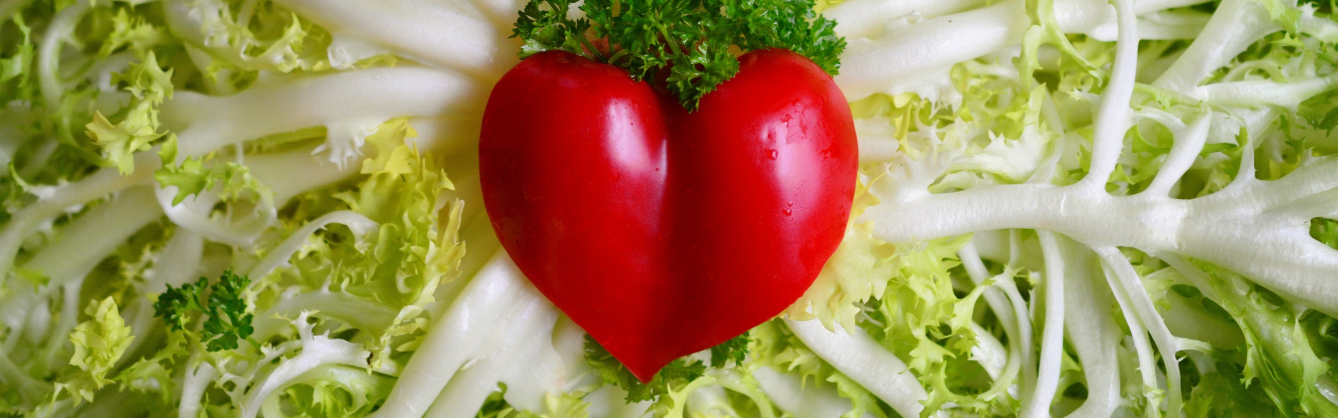 A heart-shaped pepper laying in the center of a bed of artery-like lettuce leaves