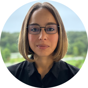 Headshot of Lina Marcella Carmona wearing glasses and a bob haircut, in a black shirt. Picture is set against a natural outdoor background