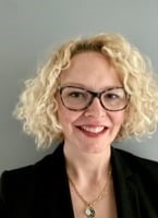 white woman with short blonde curly hair and glasses