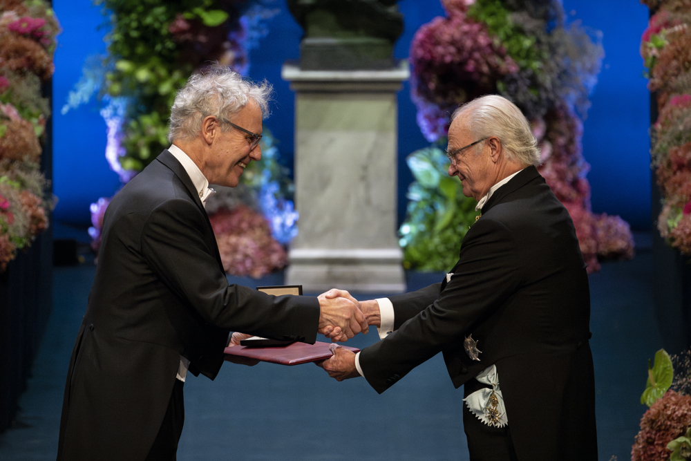 Victor Ambros in a black tuxedo being presented with his Nobel medal by King Carl XVI Gustaf of Sweden.
