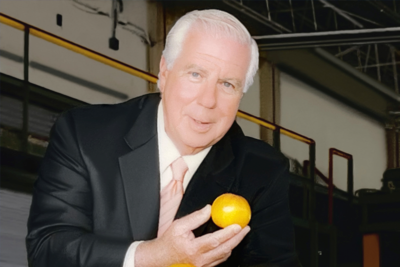 Paul J. DiMare holding a tomato above a box of DiMare tomatoes. 