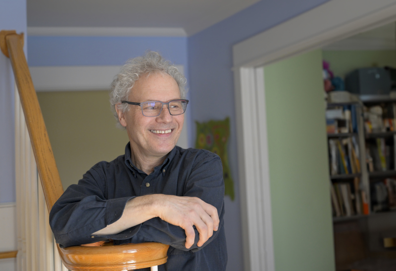 Victor Ambros leans on a stairway railing in his home