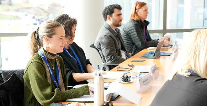 Participants sitting at a long table in front of bright windows