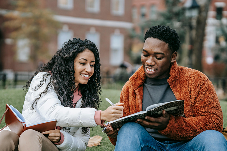 black male and female college students sitting outside reviewing a notebook